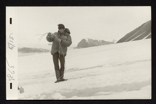 Un homme tient deux cales dans les mains, il est debout sur un glacier et fume une cigarette - mission du CNRS 1965