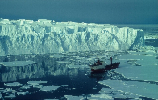 Vue prise d'hélicoptère : le Thala Dan naviguant dans un pack assez lâche près d'un très gros iceberg tabulaire.