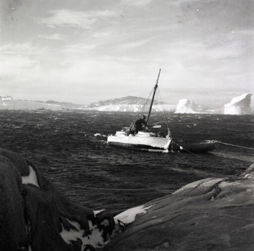 Le Skodern et une barque, sur une mer houleuse, près de la côte. A l'arrière plan, un îlot et icebergs.