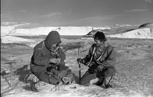 Deux hivernants, non identifiés, se préparent pour une randonnée par beau temps. En arrière-plan, l'île Jean Rostand et l'Astrolabe.