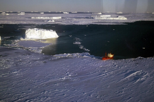 Vue prise d'hélico du Thala Dan stoppé par la banquise. Mer partiellement prise, nombreux icebergs au loin.