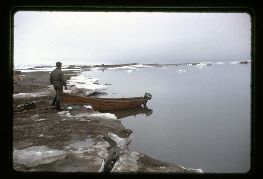 Un homme debout devant une barque dans l'eau - mission CNRS 1964 - vue 1