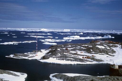 Survol vers le nord-ouest de l'île des Pétrels. Icebergs et pack à perte de vue. Le Thala Dan amarré aux Pétrels et Jean Rostand.