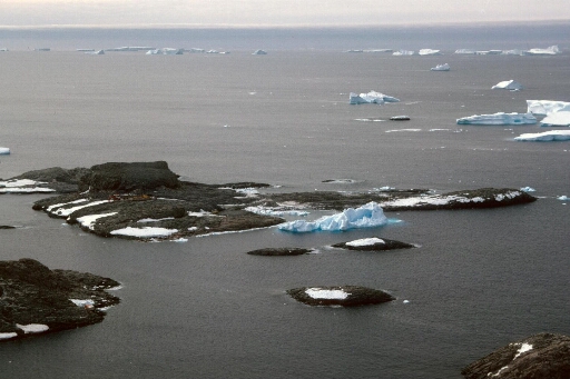 Vue aérienne de l'île du Lion sur laquelle on aperçoit les engins de travaux publics. Mer libre, nombreux icebergs à l'horizon.