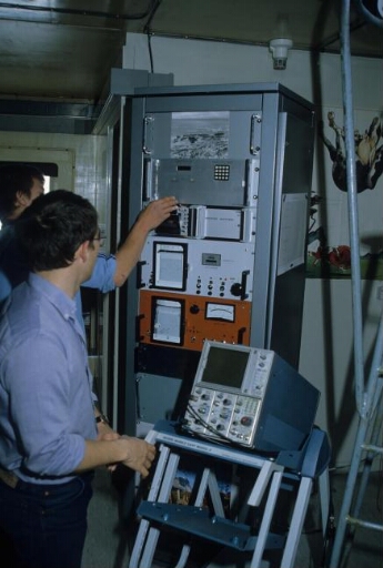 Le laboratoire de sondage ionosphérique dans le labo 1 (Bt n°25) : deux techniciens devant une baie électronique.
