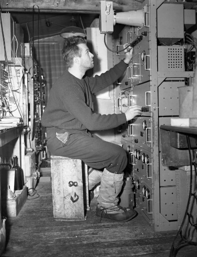 L'ingénieur Jean Bouquin assis sur une caisse devant le sondeur ionosphérique (étude des couches ionisées de la haute atmosphère).