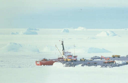 Le chantier de construction de la piste du Lion. Le Polarbjorn accosté à l'île, l'hélicoptère sur le pont. Petits icebergs dans une mer qui paraît prise.