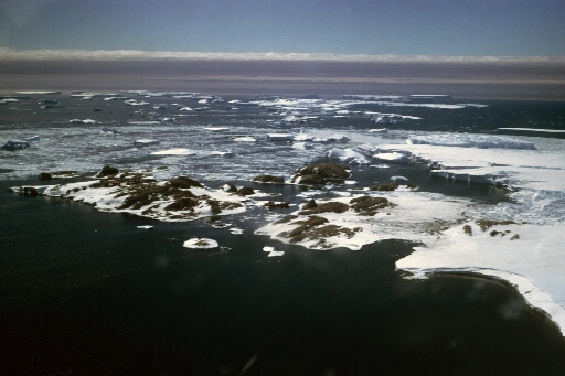 Survol, vers le nord-est, de l'archipel, du nunatak du Bon Docteur et du front de l'Astrolabe. Le Thala Dan dans le détroit.Nombreux icebergs.
