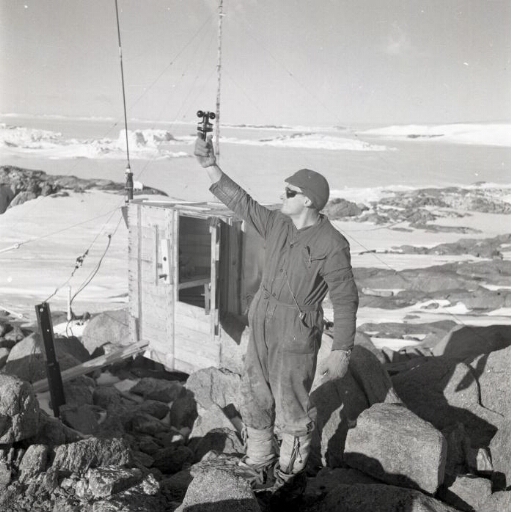 Le météorologiste André Prudhomme effectue une mesure de vent. Au loin la baie et la banquise.