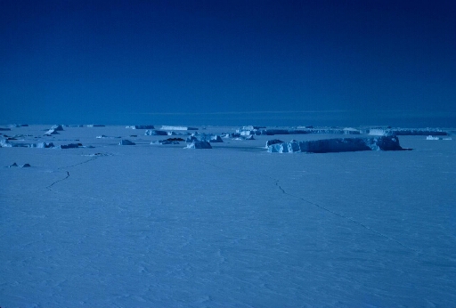 La banquise à perte de vue, nombreux icebergs. Au centre de l'image un îlot : le rocher du Débarquement.