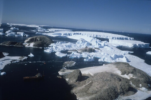 Vue aérienne vers l'est : les îles C. Bernard, Buffon et Lamarck et, au-delà, de grands icebergs tabulaires. Le Polarb Jorn ancré près des Pétrels au premier plan.