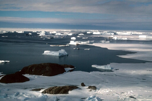 Vue aérienne vers le nord-est : l'île Claude Bernard. Mer libre puis banquise à l'horizon. Nombreux icebergs.
