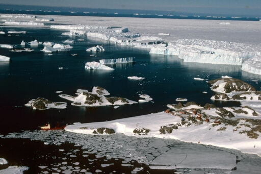 Survol, vers l'est de la pointe nord des Pétrels à laquelle le Thala Dan est amarré. Les îles proches puis les icebergs issus de l'Astrolabe.