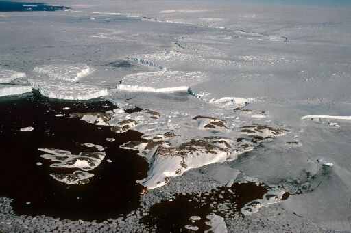 Vue aérienne à haute altitude de l'archipel en direction de l'Astrolabe et du continent. Icebergs, pack et mer libre. Le Thala Dan amarré à la pointe nord des Pétrels.