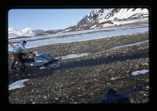 Un homme debout près d'un skidoo sur un sol rocailleux - mission CNRS 1966