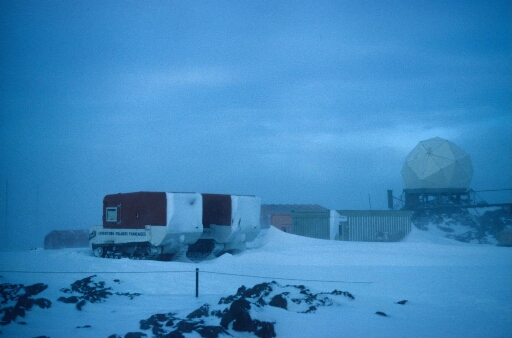 La base au cœur de l'hiver, ciel couvert, visibilité réduite. Le radôme du radar météo. Deux weasels en stationnement.