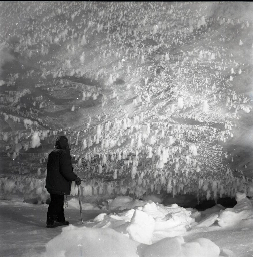 Un marcheur contemple la surface verticale d'un iceberg après une neige récente.