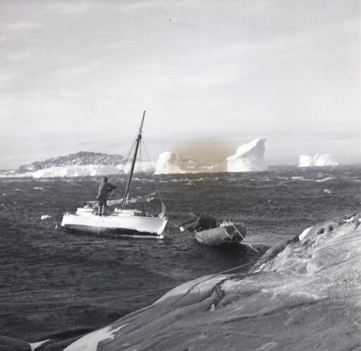 Le Skodern et une barque, sur une mer houleuse, près de la côte. A l'arrière plan, un îlot et icebergs.