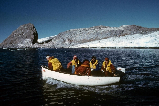 Cinq hommes à bord d'un canot naviguant en mer libre. En arrière plan, l'île Jean Rostand.