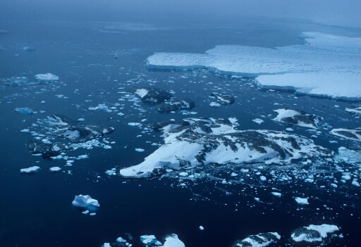 Vue aérienne vers l'est de l'archipel en direction du glacier de l'Astrolabe. Mer libre, faible luminosité. Au loin, dans la brume, le continent.