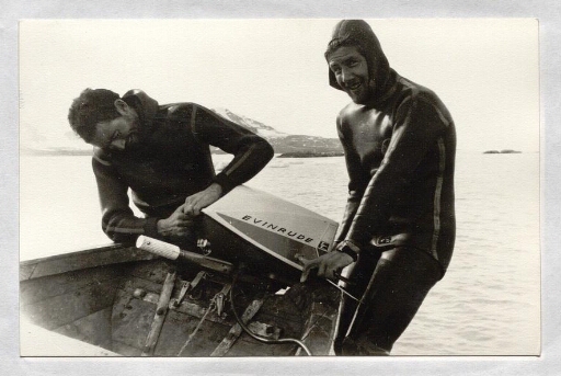 Deux hommes en tenue de plongée bouteille s'affairent près d'un moteur de bateau
