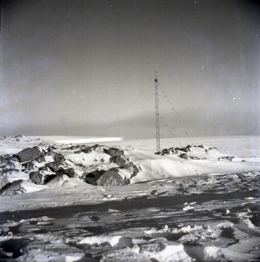 La station sous la neige. Le pylône de la radio. Plus loin, la banquise et un iceberg.