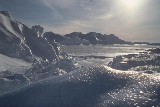 Mer gelée, icebergs et icebergs retournés. Ciel de traîne, soleil voilé.