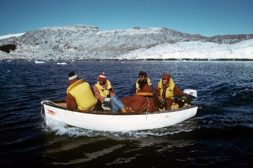 Cinq hommes à bord d'un canot naviguant en mer libre. En arrière plan, l'île Jean Rostand.