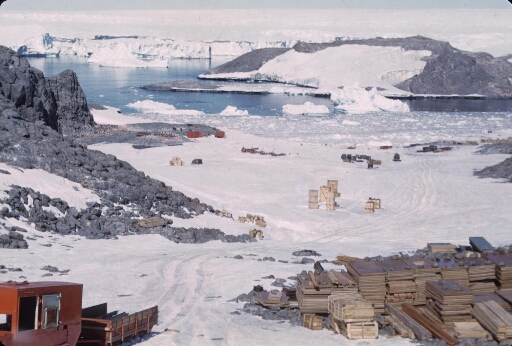 Les matériaux de construction débarqués du Norsel destinés à la construction de la base de l'AGI. A l'arrière-plan le glacier de l'Astrolabe.