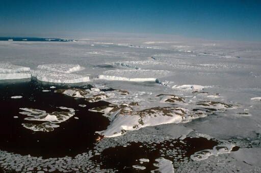 Vue aérienne à haute altitude de l'archipel en direction de l'Astrolabe et du continent. Icebergs, pack et mer libre. Le Thala Dan amarré à la pointe nord des Pétrels.