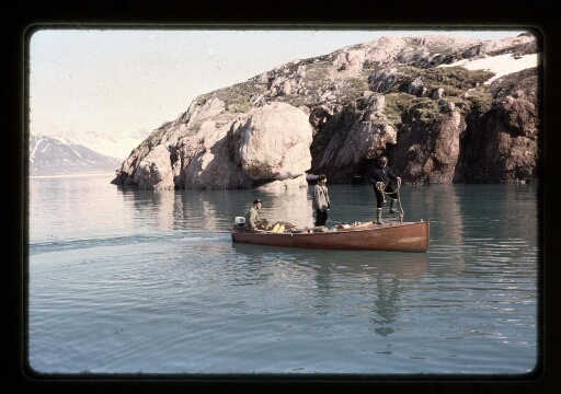 Trois hommes debout sur une petite barque en bois dans le fjord près de la base Corbel - mission CNRS 1965