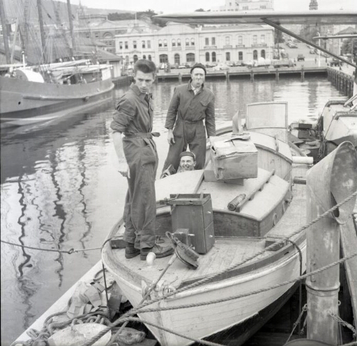 Le navire à quai dans le port de Hobart. Trois hommes, dont René Dova, sur l'une des chaloupes.