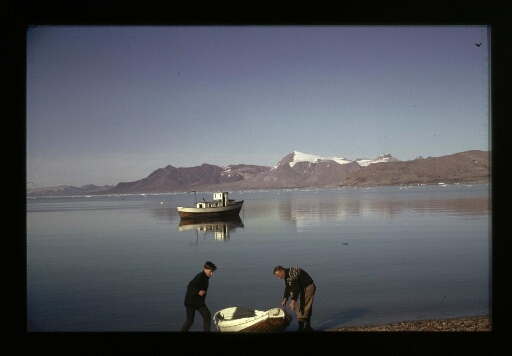 Un homme et un adolescent s'affairent autour d'une petite barque en bois en bord d'un fjord.- mission CNRS 1963