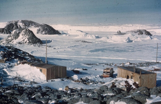 Les deux bâtiments de la base Marret et un weasel. Au loin le mont Rose sur l'île des Pétrels, l'île Lamarck puis le glacier de l'Astrolabe.