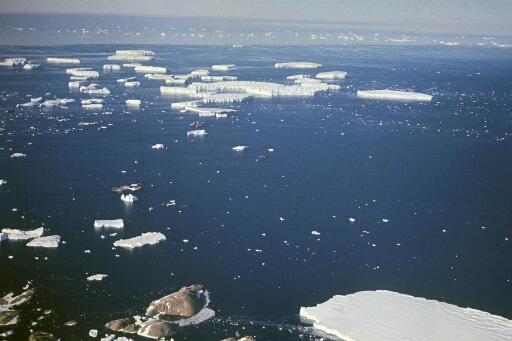 Vue aérienne vers le nord-est : les îles Buffon et Claude Bernard puis le front du glacier de l'Astrolabe. Nombreux icebergs sur une mer libre.