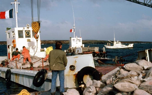 À Port aux Français (PAF), le chaland le Gros Ventre  déchargement de sacs de ciment par des hivernants volontaires, e dos Joel Drouet (mécano engin) en ciré orange FX Oury (hydrobio)