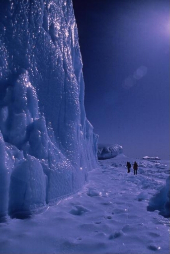 Ballade pendant l'hivernage de deux hommes sur la banquise au pied d'un iceberg. Glace et lumière d'un bleu intense.