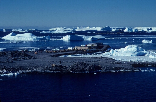 La base vie du chantier de la piste du Lion vue depuis l'île des Pétrels.  L'arrière-plan, nombreux icebergs dans une mer libre. Très beau temps.
