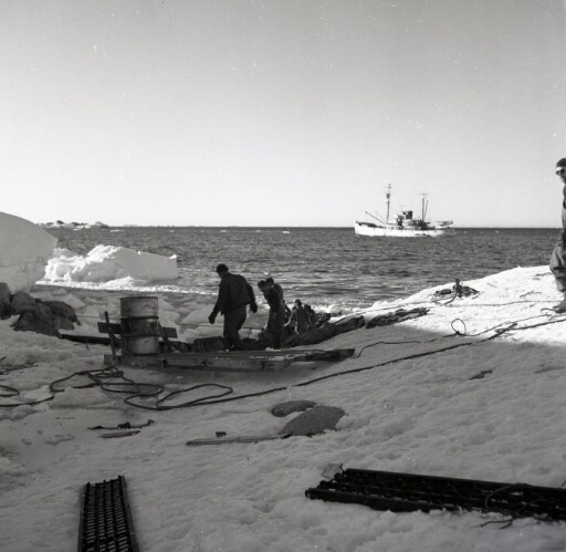 Sur le rivage, installation ou démontage des équipements du débarquement. Le Commandant Charcot au mouillage.