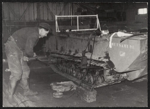 Un homme fait une réparation sur une véhicule à chenille dans une garage.