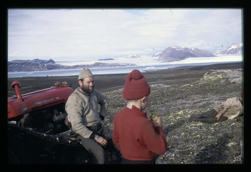 Un homme et un enfant de dos près d'un tracteur avec en arrière plan un glacier - mission CNRS 1965