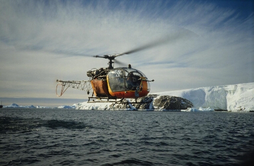 L'hélicoptère Alouette 2 survole, à basse altitude, la mer libre. En arrière-plan, les îles Buffon et Claude Bernard puis le glacier de l'Astrolabe.