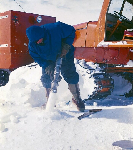 Le glaciologue Claude Lorius démoule une carotte de glace. Sno-Cat en arrière plan.