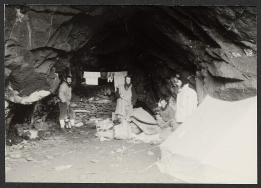 Quatre hommes à l'abri dans une grotte. Du linge étendu et une tente dépliée