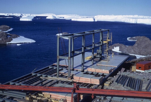 Le chantier de construction du bâtiment n°42 "logement d'hivernage". A l'arrière-plan le glacier de l'Astrolabe et de nombreux  icebergs.