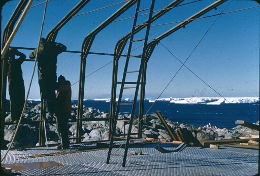 Construction de l'un des deux premiers bâtiments de la base Dumont d'Urville. Au loin les icebergs du front de l'Astrolabe.
