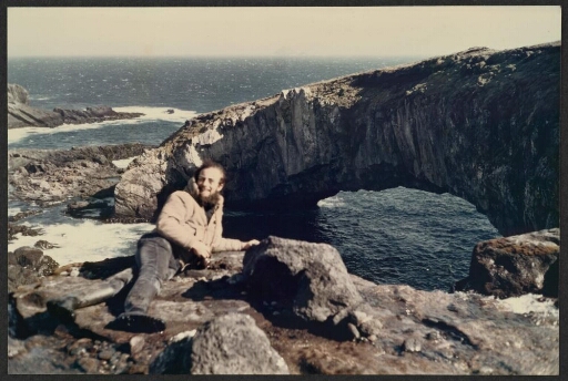 Un homme allongé sur le haut d'une falaise cotière, devant une arche de pierre