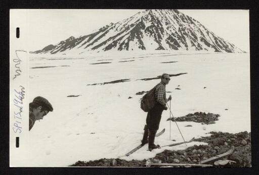 Un homme debout sur des ski de fond et un homme qui fume une cigarette devant une étendue de neige en bas d'une montagne- mission du CNRS 1966