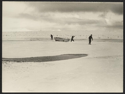 Trois personnes skient autour d'une véhicule à chenille bloquée dans la glace
