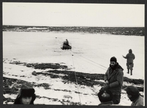 Un groupe d'homme tire une barque a moteur prise dans la glace à l'aide de corde